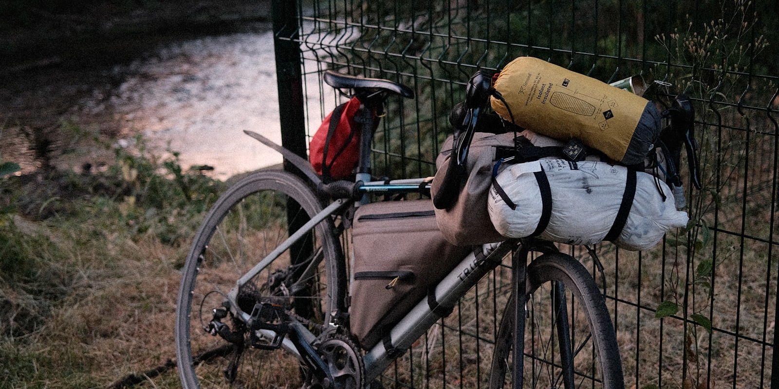 Vélo de bikepacking chargé, appuyé contre une clôture au crépuscule