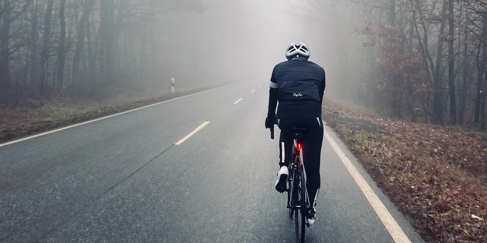 Cycliste en veste noire sur une route mouillée par temps de brume
