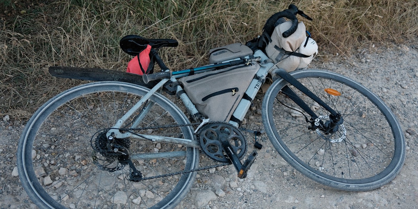 Vélo de gravel chargé de sacoches, posé au bord d'un chemin caillouteux