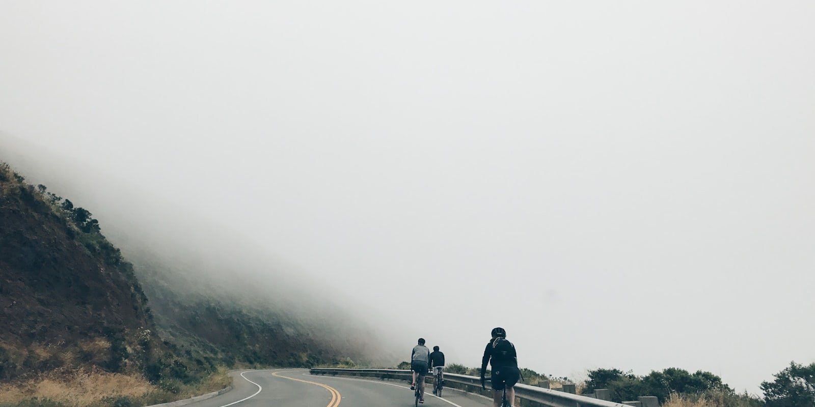 Trois cyclistes roulant en file sur une route côtière dans la brume