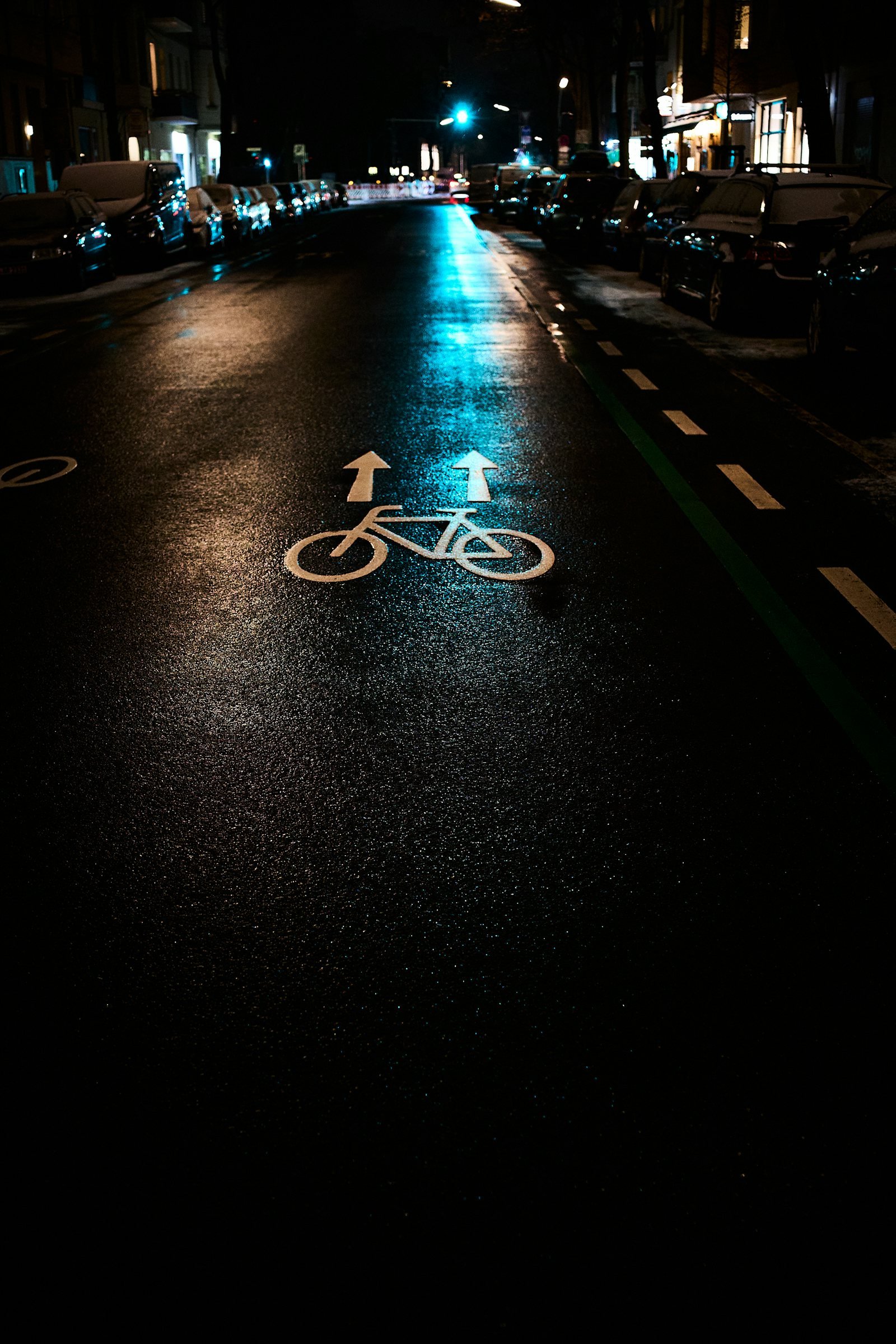 Piste cyclable détrempée la nuit, reflets bleus et orangés sur l'asphalte