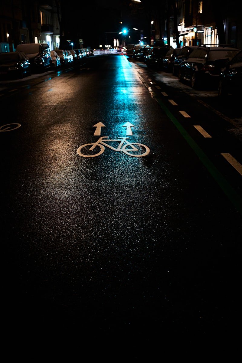 Piste cyclable marquée au sol, de nuit, sur une chaussée mouillée qui reflète les lumières de la rue