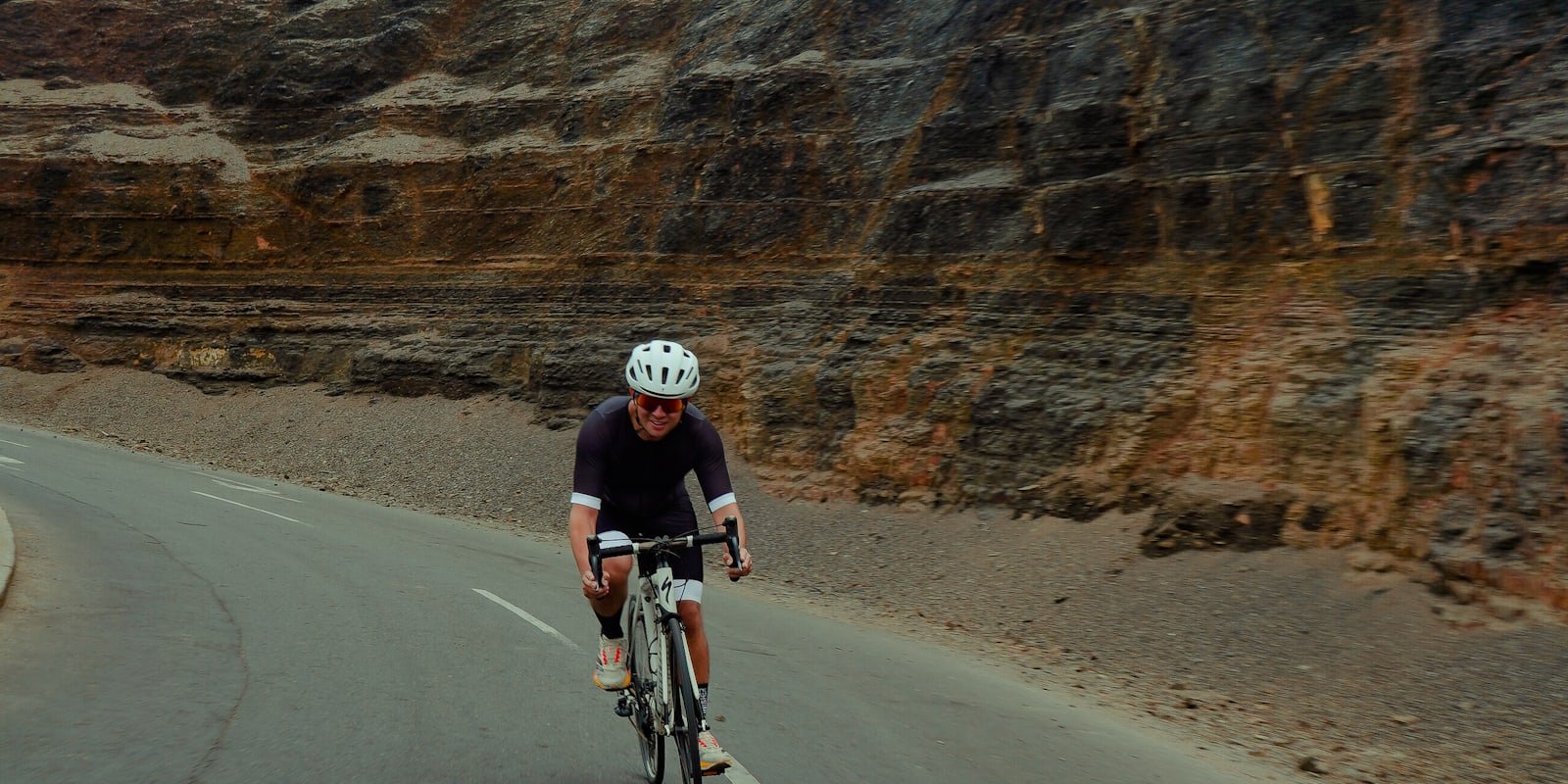 Cycliste sur une route taillée dans la falaise, exposée au vent