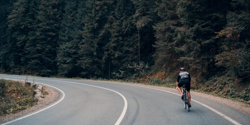 Route sinueuse traversant une forêt, un cycliste au loin